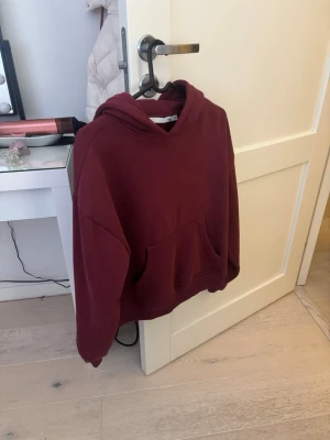 Vinröd hoodie med magficka - Säljer en vinröd hoodie i mjukt bomullsmaterial. Hoodien har en stor huva och en klassisk magficka framtill. Oversized passform och ribbade muddar vid ärmslut och nederkant. Perfekt för en chill och avslappnad stil.