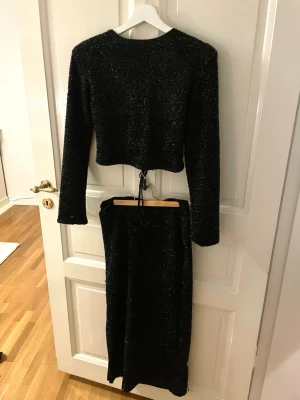 Glittrigt set!!! - Snyggt svart set från Bikbok FULL med glitter!!✨ setet har snörningar som snygga detaljer , toppen i ryggen men man kan använda och ha som bolero, och kjolen har slits. Storlek M.  Obs. Få lösa trådar förekommer.