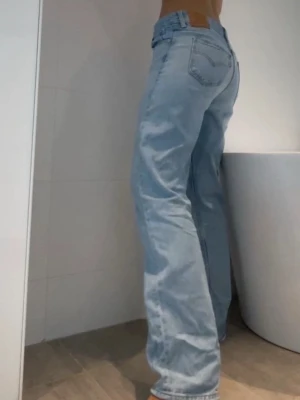 Vintage Levi's ljusblå jeans - Vintage jusblå Levi's jeans med straight passform och femficksmodell. Jeansen har låg midja och är tillverkade i slitstark denim av bomull. Perfekta för en avslappnad och trendig look.