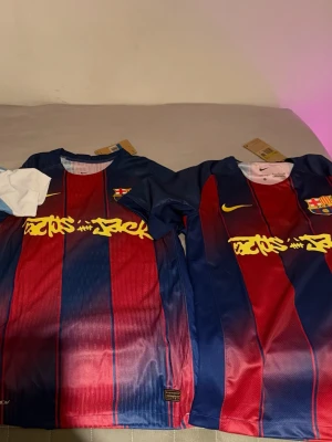 FC Barcelona x Nike matchtröja - Säljer en FC Barcelona matchtröja i samarbete med Nike och Cactus Jack. Tröjan har klassiska blå och röda vertikala ränder, gul Nike-logga och klubbmärke på bröstet samt Cactus Jack-tryck över bröstet. Perfekt för dig som älskar fotboll och streetwear.