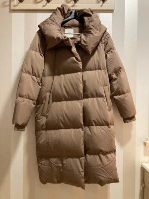  Lång dunjacka med luva - Snygg brun beige dunjacka med stor luva. Bra skick använde fåtal gånger