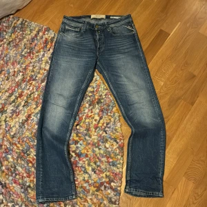 Blå raka jeans från replay - Säljer ett par klassiska blå jeans från Replay med raka ben och normal passform. Jeansen har fem fickor, gylf med dragkedja och subtila slitningar framtill för en avslappnad look. Perfekta till vardags och lätta att matcha.