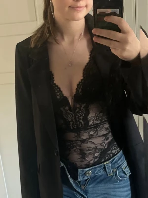 Svart spetsbody från H&M - Snygg svart body från H&M i genombruten spets med djup V-ringning och tunna axelband. Spetsdetaljer och transparent material ger en trendig look. Pris diskuteras gärna! 