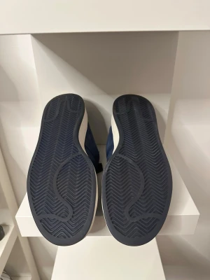 Marinblå adidas Campus sneakers - Snygga marinblå adidas Campus sneakers med klassiska tre ränder på sidan. Ovandelen är i mocka och sulan är vit med mörkblå yttersula. Skorna har snörning och en låg profil som passar till många olika stilar.