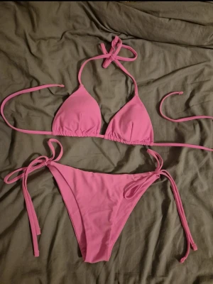 Rosa trekantsbikini med knytband - Säljer en snygg rosa bikini med trekantsmodell på överdelen och knytband både i nacken, ryggen och på sidorna av underdelen. Klassisk och enkel design som passar perfekt till stranden eller poolen. Materialet känns mjukt och stretchigt för skön passform. Passar även S! 