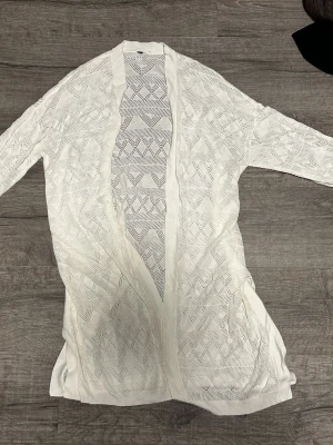 Vit lång öppen stickad kofta - Vit lång kofta med öppen front och stickat mönster i geometriska former. Lätt och luftig, perfekt att slänga över en topp. Långa ärmar och ribbade kanter ger med öppning på slutet. Vet tyvärr inte var den är ifrån eller vilken storlek men skulle gissa på att det är storlek M ( jag brukar bära storlek xs/s). SÅ VAR DEN ÄR IFRÅN ÄR INTE SANT!