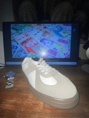 MAISON MARGIELA - Stilrena sneakers i vitt och beige med snygga mockadetaljer och klassisk snörning. Skon har en rund tå och platt sula i brunt gummi. Perfekt för dig som gillar en clean och tidlös look. Har aldrig använt.