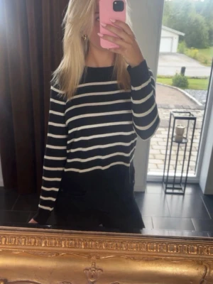 Svartvit randig stickad tröja - Svart stickad tröja med vita horisontella ränder. Tröjan har rund halsringning och långa ärmar. Modellen är rak och enkel, perfekt för en stilren look. Materialet ser ut att vara mjukt och lättstickat.