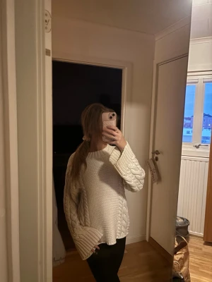 Vit stickad tröja med flätmönster - Mysig vit stickad tröja med breda flätmönstrade ärmar och grovstickad framsida. Tröjan har en avslappnad passform och långa ärmar, perfekt för kyliga dagar. Enkel att matcha med både jeans och leggings.