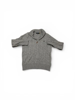 Grå kabelstickad tröja Polo Ralph Lauren - Snygg grå kabelstickad tröja från Polo Ralph Lauren med halv dragkedja och hög krage. Tröjan har ribbade muddar och en liten broderad logga på bröstet. Perfekt för lager på lager och en chill men ändå stilren look.