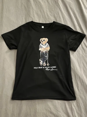 Ralph Lauren T-shirt  - Svart t-shirt med klassisk Polo Bear-tryck från Ralph Lauren. Skick 10/10. Storleken är M -> men passar mer xs/s 