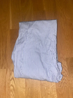 Randiga pyjamasbyxor i bomull - Snygga pyjamasbyxor i vitt och ljusblått randigt mönster. Byxorna har resår i midjan och är gjorda i mjuk bomull, perfekta för att chilla hemma eller sova bekvämt i.