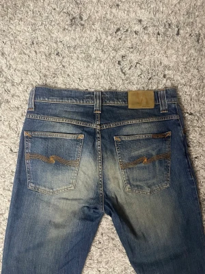 Blå jeans från Nudie Jeans - Säljer ett par klassiska blå jeans från Nudie Jeans. Modellen heter Grim Tim och storleken är W31 och L34. Nypris ligger på över 1600kr! Det finns inga defekter på jeansen.