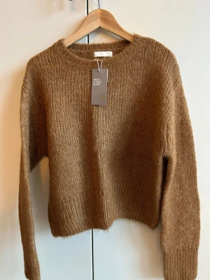 Brun stickad tröja från H&M - Det perfekta mysiga basplagget för hösten! 🍂 Helt ny tröja från H&M Premium Quality i en vacker varmbrun färg (tawny brown). Den är gjord i en varm ull- och alpackablandning med en härlig texturerad, fluffig finish. Ribbstickade detaljer vid halsringning och nederkant. Helt oanvänd med originaletiketterna kvar. Axel 45 cm, längd 50 cm 