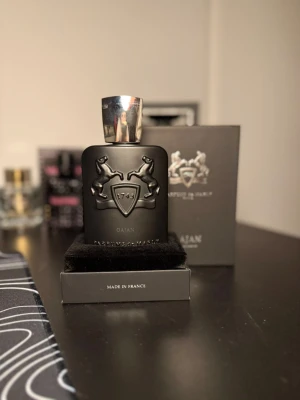 Parfums de Marly Oajan EdP 125ml - Lyxig parfym från Parfums de Marly, Oajan Eau de Parfum, i en elegant mörk kartong med silverdetaljer och logga. Flaskan rymmer 125 ml och doften är känd för sina varma, kryddiga och söta toner. Perfekt för dig som vill sticka ut med en exklusiv signaturdoft. Ungefär 100ml kvar den är en R#plica 
