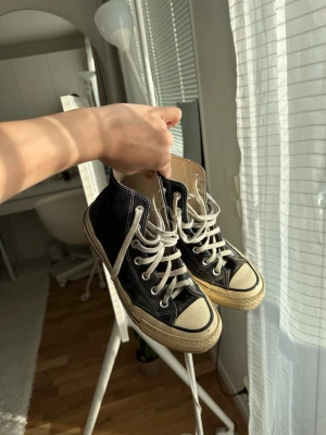 Svarta high top converse sneakers med snörning - Klassiska svarta high top sneakers med vit sula och tå, samt vita snören. Skorna har en retro vibe och är tillverkade i canvas med detaljer i gummi. Perfekta för en avslappnad streetstyle-look.