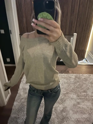 Beige off shoulder stickad tröja - Snygg beige stickad tröja med off shoulder-design och långa ärmar. Tröjan har bred ribbstickad mudd vid ärmslut och nederkant. Perfekt för dig som gillar en avslappnad men trendig stil. Materialet ser mjukt och bekvämt ut.