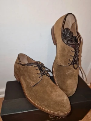 Bruna mocka loafers från Massimo Dutti - Bruna loafers från Massimo Dutti i mjuk mocka med klassisk rund tå och platt sula. Skorna har snörning i mörkbrunt och stilren design som passar till många olika looks. Perfekta för dig som gillar en clean och tidlös stil.