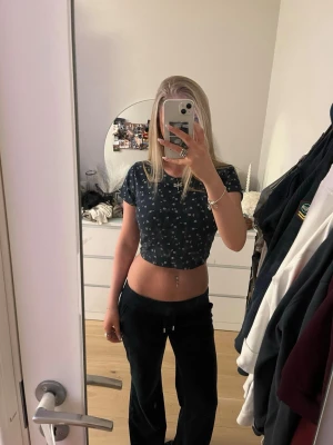 Croppad top Hollister - Snygg mörkblå croppad topp med små vita blommor. T-shirten har korta ärmar och rund halsringning. Perfekt till jeans eller kjol för en trendig look. Materialet känns mjukt och stretchigt, storlek S.