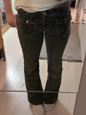 Svarta bootcut jeans med fickdetaljer - Snygga svarta bootcut jeans från Gina Tricot , med snygga fickor framtill och dekorativa knappar. Jeansen har en klassisk femficksdesign och är tillverkade i ett mjukt denimtyg. Perfekta för dig som gillar en avslappnad men trendig look. Passform 152cm 