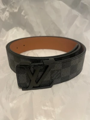 Svart Rutigt bälte 110cm - Svart bälte som är rutigt med en svart logga. 110cm. 