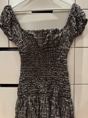 Svartvit rutig klänning med puffärm - Söt svartvit/beige rutig klänning med smockad överdel. Använd väldigt sparsamt. 