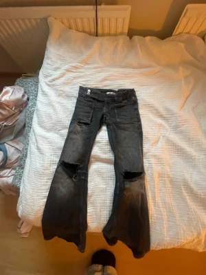 Snygga jeans - Ett par snygga mörkgrå/svarta jeans med slitningar framtill och bootcut/flared passform. Låg midja och stretchigt tyg som sitter fint. Använda men i gott skick.Är i storlek 140💕