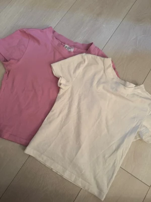 2-pack basic t-shirts från H&M Divided - Två basic t-shirts från H&M Divided i storlek XS. Ena t-shirten är ljusrosa och den andra är vit. Båda har rund halsringning och korta ärmar. Perfekta till vardags och lätta att matcha med olika outfits.