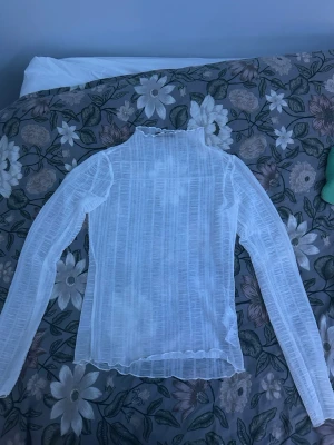 Vit mesh polotopp från Gina Tricot - Säljer en transparent vit polotopp från Gina Tricot i meshmaterial. Toppen har lång ärm, hög hals och ett subtilt randigt mönster i tyget. Perfekt att styla lager på lager eller med ett snyggt linne under.