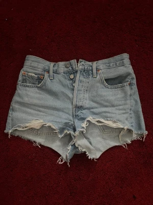 Levi's ljusblå denimshorts  - Säljer ett par ljusblå denimshorts från Levi's med hög midja och råa, fransiga kanter. Klassisk femficksmodell med knappgylf och Levi's patch bak. Perfekta för sommaren och ger en avslappnad vibe. Helt nya och oanvända.