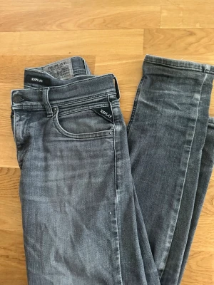 Replay grå slim jeans - Snygga grå jeans från Replay i slim passform. Jeansen har klassisk femficksdesign, svarta Replay-detaljer och diskret tvättad look. Tillverkade i mjuk bomullsdenim med stretch för extra komfort. 158cm.