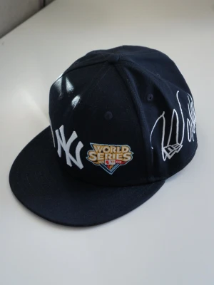 New York Yankees World Series keps - Mörkblå snapback-keps från New Era med New York Yankees-logga framtill, World Series-märke och broderad text 'World Series Champions' på sidan. Klassisk rak skärm och broderade ventilationshål. Perfekt för dig som gillar streetwear och baseball.