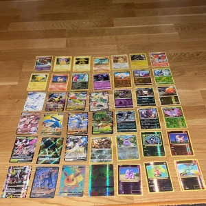 Pokémonkort samling - En färgstark samling Pokémonkort med både klassiska och moderna motiv, inklusive flera holografiska och sällsynta kort. Perfekt för dig som älskar Pokémon och vill utöka din samling eller börja spela med vänner. Passar både samlare och fans av Pokémonvärlden.