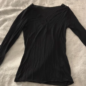 Svart långärmad topp med spetsdetaljer - Säljer en svart långärmad topp med v-ringning och snygga spetsdetaljer vid halsringningen. 