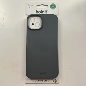 Holdit Silicone Case för iPhone 14/13 - Stilrent mörk grått silikonfodral från Holdit, anpassat för iPhone 14 och 13. Ger ett bra grepp och skydd mot repor och stötar. Produkten är ny i förpackning och fri från synliga defekter eller slitage.