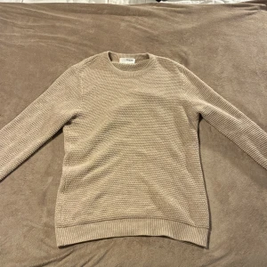 Beige stickad tröja från Selected Homme - Säljer en beige stickad tröja från Selected Homme. Tröjan har en grovstickad struktur, rund halsringning och ribbade muddar vid ärmslut och nederkant. Perfekt för lager-på-lager och chillare dagar.