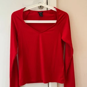 Ny röd  ribbad långärmad topp Lindex - Riktigt snygg röd långärmad topp från Lindex med v-ringning och ribbad struktur. Toppen har en smickrande passform och är gjord i ett mjukt, stretchigt material som känns skönt mot huden. Perfekt att styla med jeans eller kjol för en cool look.