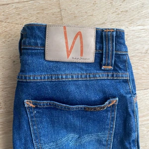 Blå jeans från Nudie Jeans - Snygga blå jeans från Nudie Jeans med klassisk femficksdesign och kontrastsömmar. Jeansen har en rak passform och är tillverkade i slitstarkt denim med Nudie-logga på bakfickan och läderpatch i midjan. Perfekt för dig som gillar stilrena och tidlösa jeans.