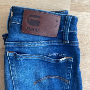 Blå skinny jeans från G-Star RAW - Snygga blå jeans från G-Star RAW med klassisk femficksdesign och brunt läderpatch bak i midjan. Jeansen har smal passform och diskreta slitningar för en cool look. Broderad logga på bakfickan och kontrastsömmar ger extra detaljer.