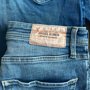 Blå jeans från Jack & Jones - Snygga blå jeans från Jack & Jones med klassisk femficksdesign och läderpatch bak i midjan. Jeansen har en rak passform och är tillverkade i slitstarkt denim med lätt tvättad look och subtila detaljer på bakfickorna.