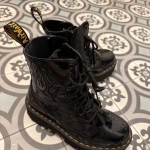 Svarta Dr. Martens boots lack chunky - Säljer ett par svarta Dr. Martens boots i glansigt lackskinn med klassisk gul söm runt sulan. Skorna har snörning, dragkedja på sidan och kraftig plattformsula. Perfekta för dig som vill sticka ut med en edgy stil.