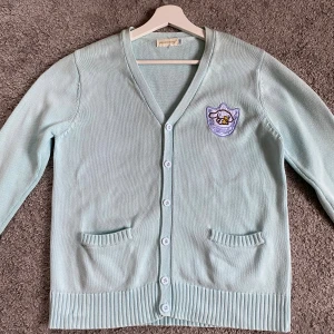 Ljusblå kofta från yujian.niong, M - Supersöt ljusblå kofta med broderad Sanrio patch på bröstet, v-ringning och knappar hela vägen. Två små fickor framtill och ribbade muddar ger en chill vibe. Perfekt för lager-på-lager och passar till allt. Har för mig att den kostar 300 kr ny pris.