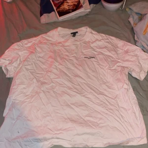 Vit t-shirt från Calvin Jungle XXL - Vit t-shirt i storlek XXL från Calvin Jungle med stor svart grafisk print på ryggen och liten logga framtill. Klassisk rund hals och korta ärmar. Skön och enkel stil, perfekt till jeans eller shorts. Materialet känns som bomull.