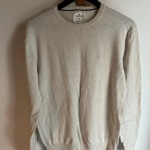 Beige stickad tröja från Springfield - Säljer en stilren beige stickad tröja från Springfield i storlek M. Tröjan har rund halsringning, diskret broderad logga på bröstet och ribbade muddar vid ärmslut och nederkant. Perfekt för lager-på-lager och enkel att matcha.