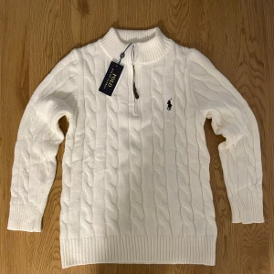Vit stickad half zip tröja Polo Ralph Lauren  - Vit kabelstickad tröja från Polo Ralph Lauren med half zip och ribbad krage. Tröjan har långärmad passform och klassisk broderad logga på bröstet. Perfekt för dig som gillar stilren och tidlös design med premiumkänsla.  jag har den i storlek M och S