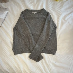 Grå stickad tröja från Dagmar - Mysig grå stickad tröja från Dagmar i storlek M men passar som XS. Tröjan har rund hals, ribbade muddar och långärmade ärmar. Perfekt för kyliga dagar och enkel att matcha med jeans eller kjol. Snygg och stilren design som funkar året runt.