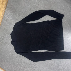 Svart ribbad polotröja från Cubus - Svart polotröja från Cubus i storlek S. Tröjan är ribbad och har lång ärm med en tight passform. Perfekt att styla med jeans eller kjol för en clean look. Materialet är mjukt och stretchigt, vilket gör den skön att bära under kyliga dagar.