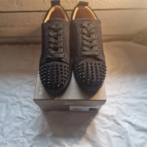 Christian Louboutin svarta sneakers med nitar - Svarta sneakers från Christian Louboutin i mocka med coola svarta nitar på tån. Skorna har snörning och en klassisk rund tå. Lyxig känsla och edgy look, perfekt för dig som vill sticka ut med din stil.