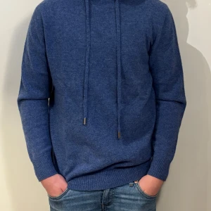 Blå marinoulls hoodie med snörning ny - Snygg blå hoodie med långa ärmar och huva. Tröjan har snörning framtill och är tillverkad i ett mjukt stickat material som känns skönt mot huden. Perfekt för dig som gillar en chill och enkel stil.