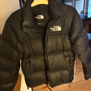 Svart pufferjacka från The North Face - Säljer en svart pufferjacka från The North Face med klassisk logga på bröstet och ryggen. Jackan har hög krage, dragkedja framtill och är riktigt dunig och varm. Perfekt för kalla dagar. Fint skick☺️